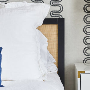 White bedding styled with an indigo lumbar, a white dresser with brass hardware, and brass base table lamp.
